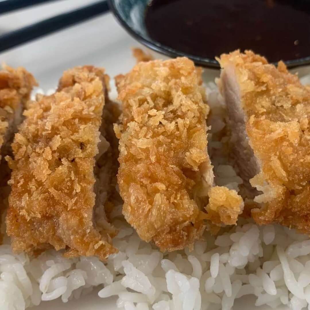 Chicken Katsu square pic on a bed of rice with katsu sauce and chopsticks in the background.