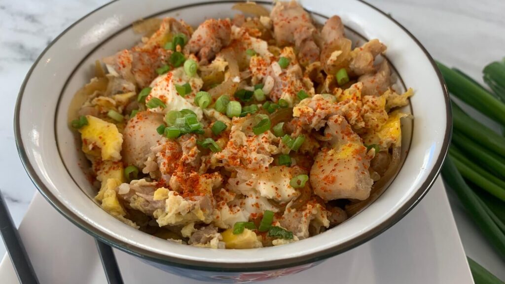 Oyakodon in a Japanese bowl with chopsticks and green onions in the background
