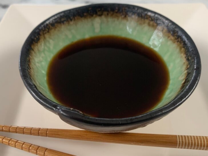 Ponzu sauce in a Japanese ramekin with brown chopsticks in the background.