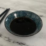 Unagi sauce in a blue Japanese ramekin with black chopsticks in the background.