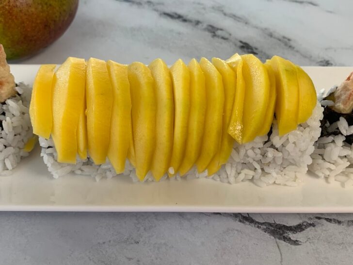 Mango sushi roll on a sushi plate with a mango in the background