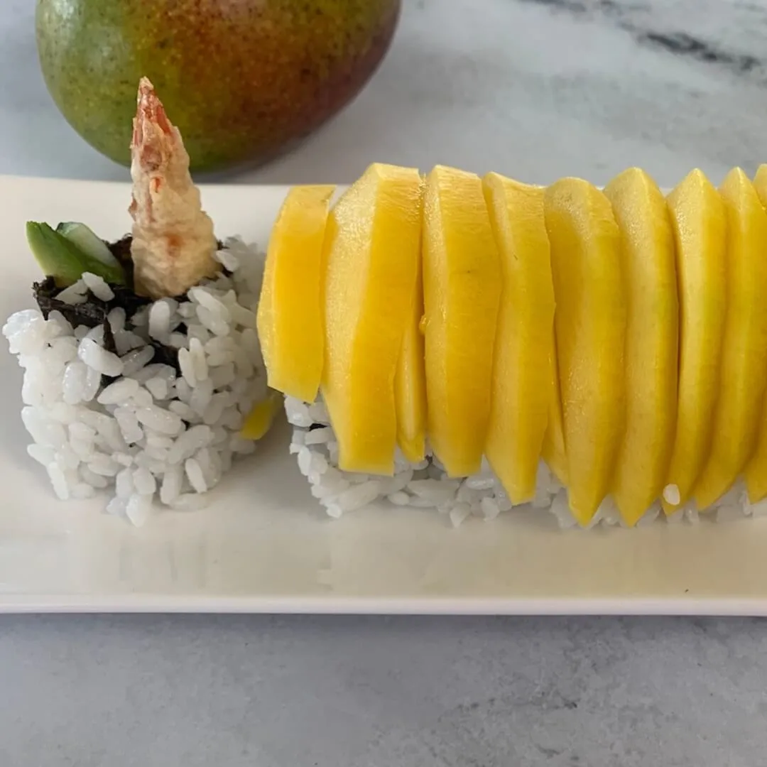 Mango roll sushi on a white sushi plate with a mango in the background