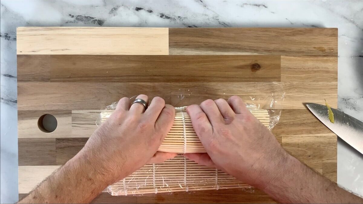 Use a sushi mat to press the mango slices onto the top of the mango roll. 