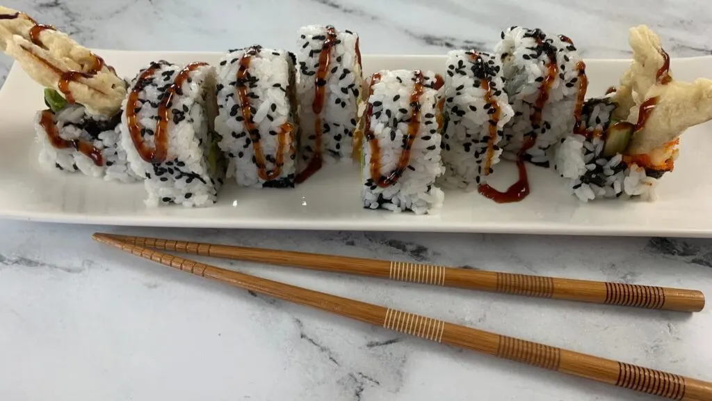 Spider roll on a white sushi plate drizzled with unagi (eel) sauce.