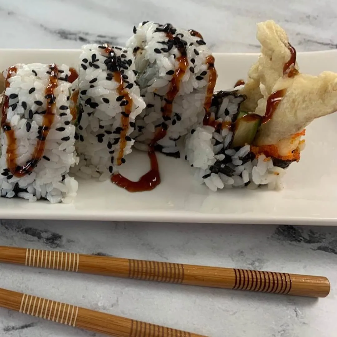 Spider roll square photo on a white sushi plate with chopsticks in the background.