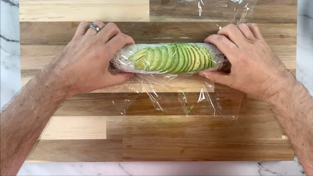 Cover the sliced avocado that is draped over the top of the caterpillar roll with plastic wrap.  This makes the roll easier to cut and helps the avocado slices to stay on the roll. 