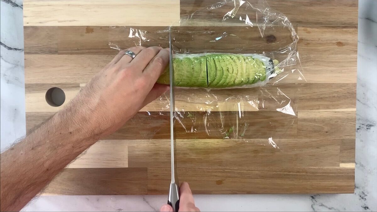 Cut the avocado roll through the plastic.  The plastic wrapping can then be removed after cutting the roll. 