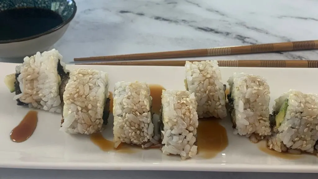 Unagi (eel) roll horizontal pic on a white plate with chopsticks and a ramekin of soy sauce.