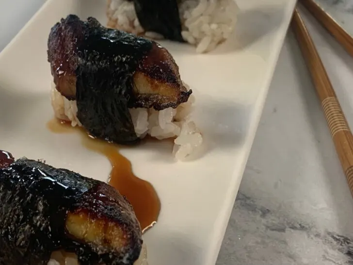 Unagi (eel) nigiri sushi on a white sushi platter with chopsticks in the background.