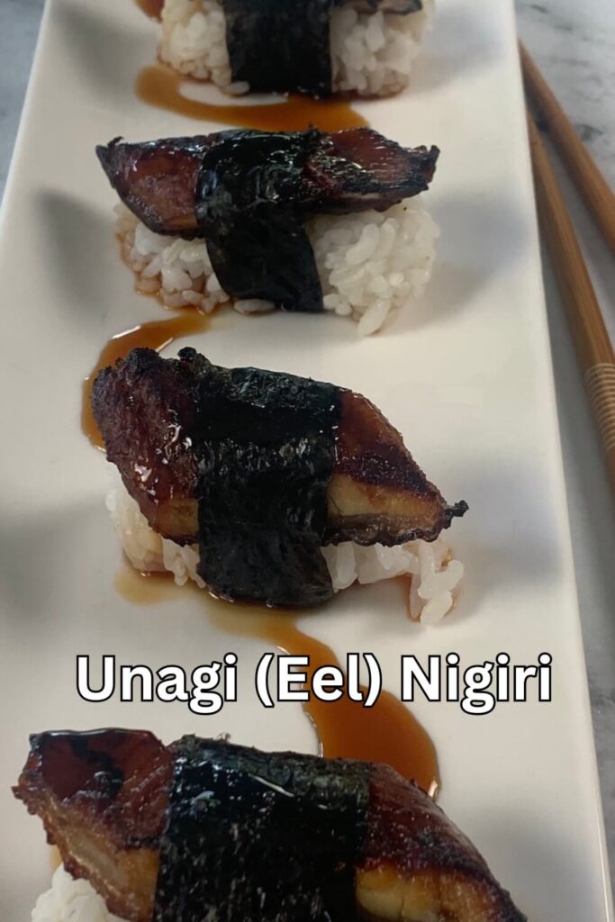 Vertical unagi (eel) nigiri drizzled with unagi sauce on a white sushi plate.