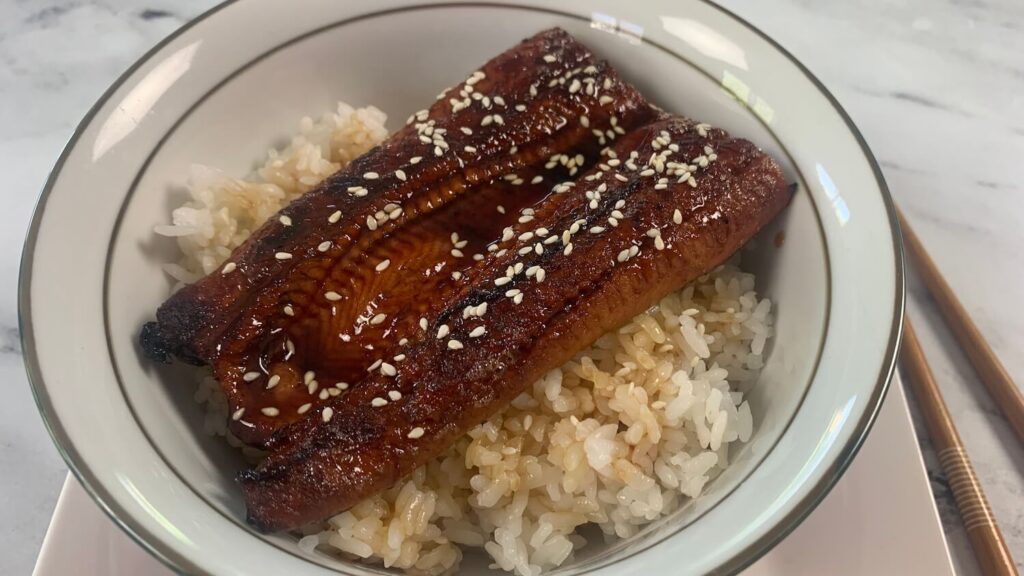 Unagi don horizontal photo in a Japanese bowl with chopsticks in the background. 