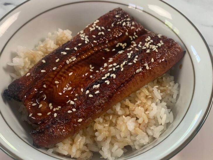 Unagi don horizontal photo in a Japanese bowl with chopsticks in the background.