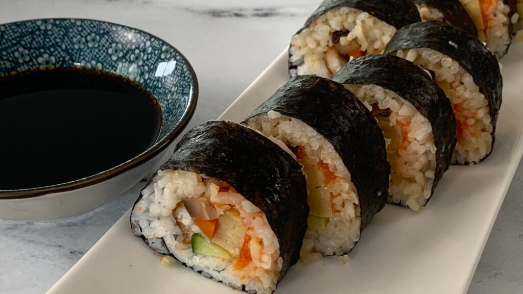 Futomaki horizontal pic arranged on a white sushi plate with a ramekin of soy sauce in a Japanese bowl in the background.