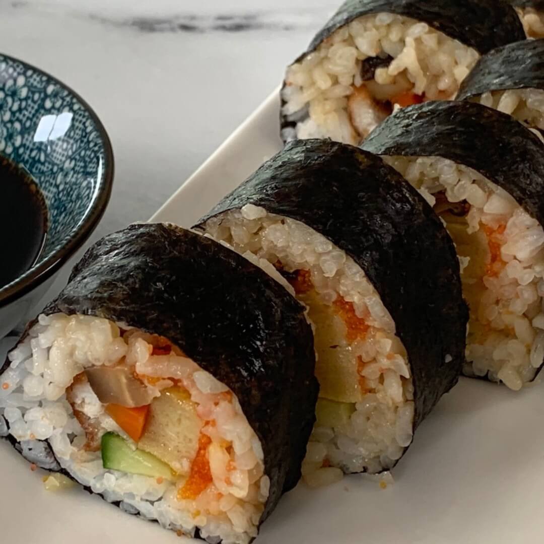 Futomaki sushi square pic on a white sushi platter with a ramekin of soy sauce in the background.