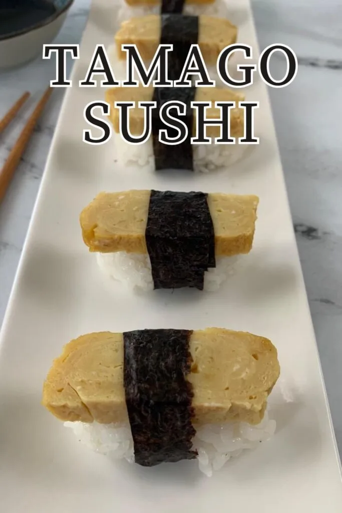 Tamago sushi on a white sushi platter with chopsticks and a ramekin of soy sauce in the background.