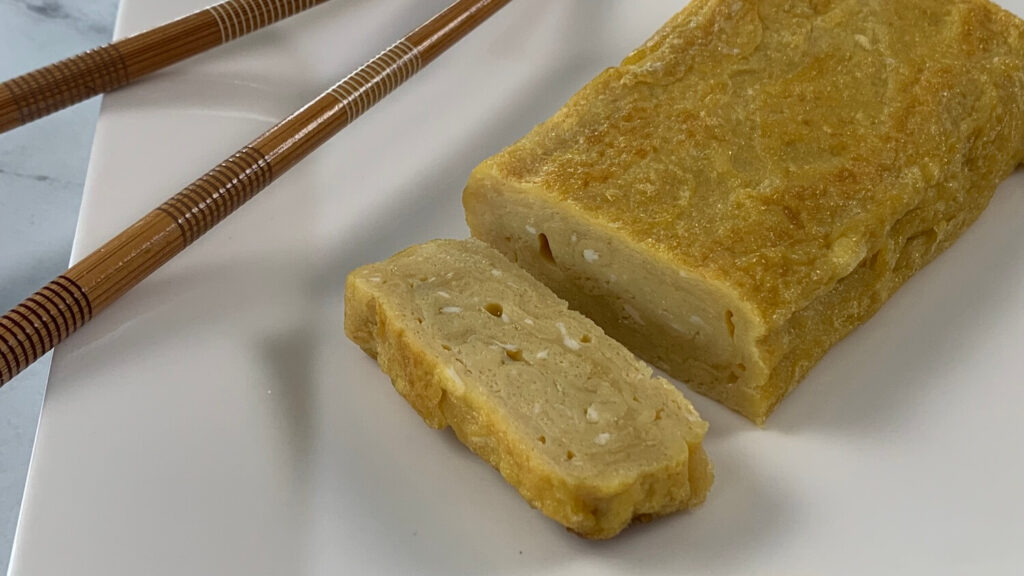 Tamagoyaki on a white plate with chopsticks on the corner of the plate.