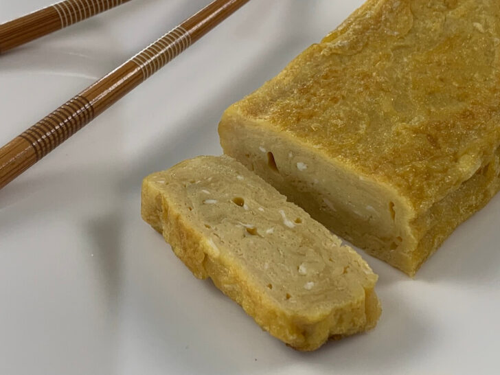 Tamagoyaki on a white plate with chopsticks on the corner of the plate.