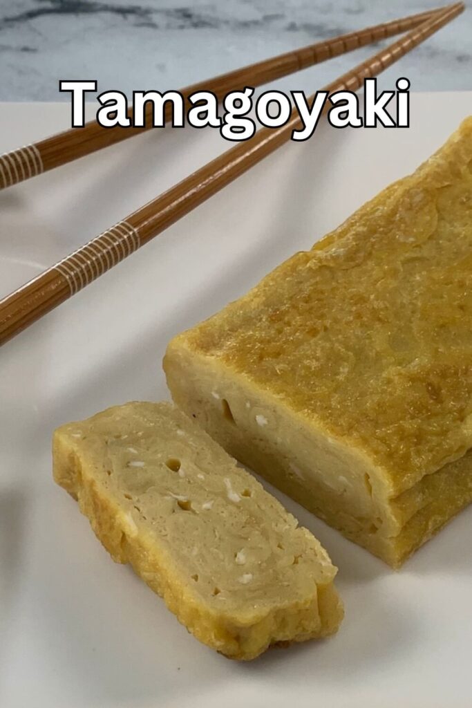 Tamagoyaki vertical pic on a white plate with brown chopsticks in the background.