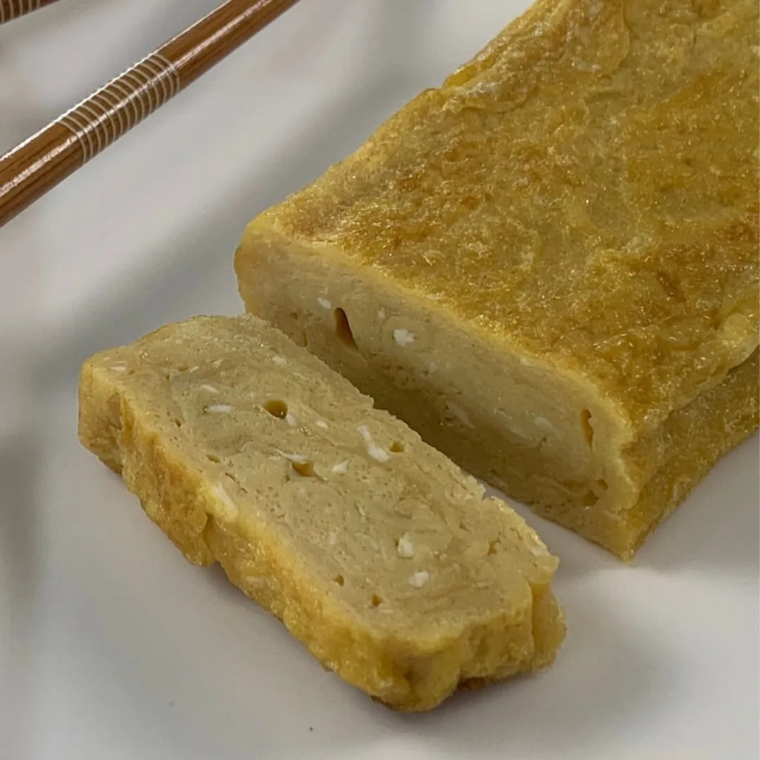 Tamagoyaki square pic on a white plate with brown chopsticks in the background.