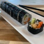 Chicken teriyaki roll on a white sushi plate and black chopsticks in the background.