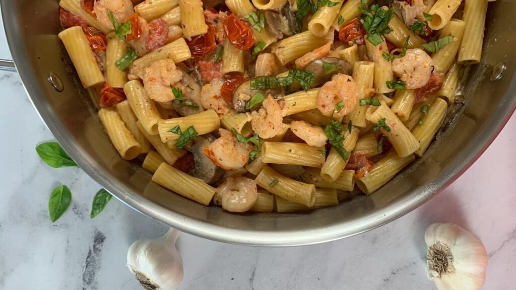 Boursin cheese pasta with shrimp horizontal pic shown with garlic bulbs and basil leaves in the background.