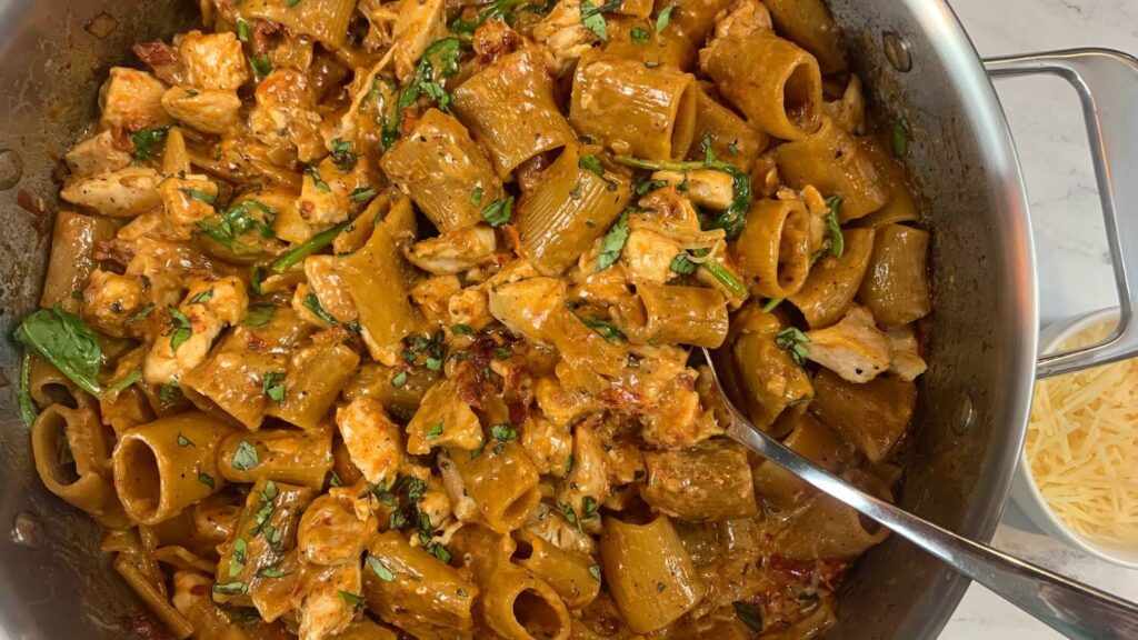 Marry me chicken pasta horizontal pic with a ramekin of parmesan cheese in the background.