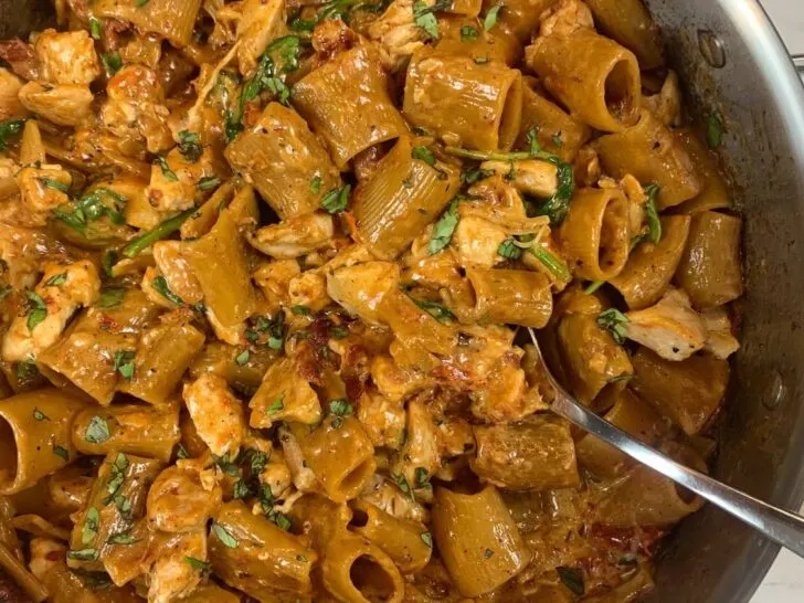 Marry me chicken pasta horizontal pic with a ramekin of parmesan cheese in the background.