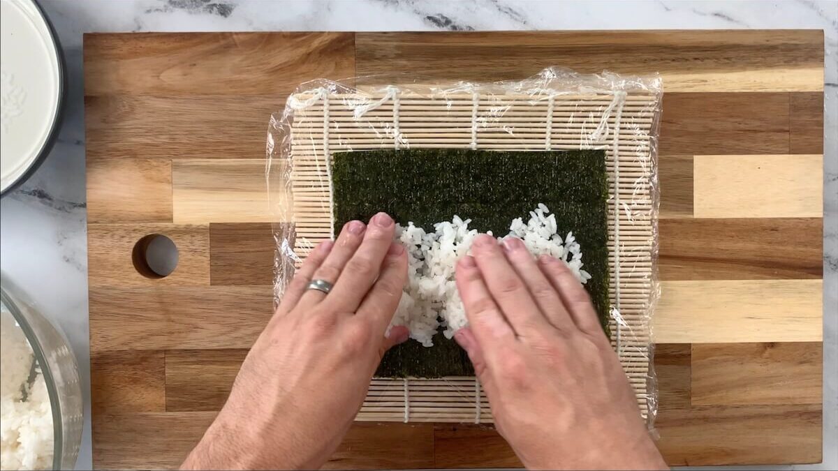 Press sushi rice onto the nori sheet leaving the top portion of the nori sheet uncovered.