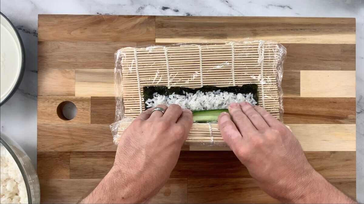 Roll the cucumber roll using the sushi mat.