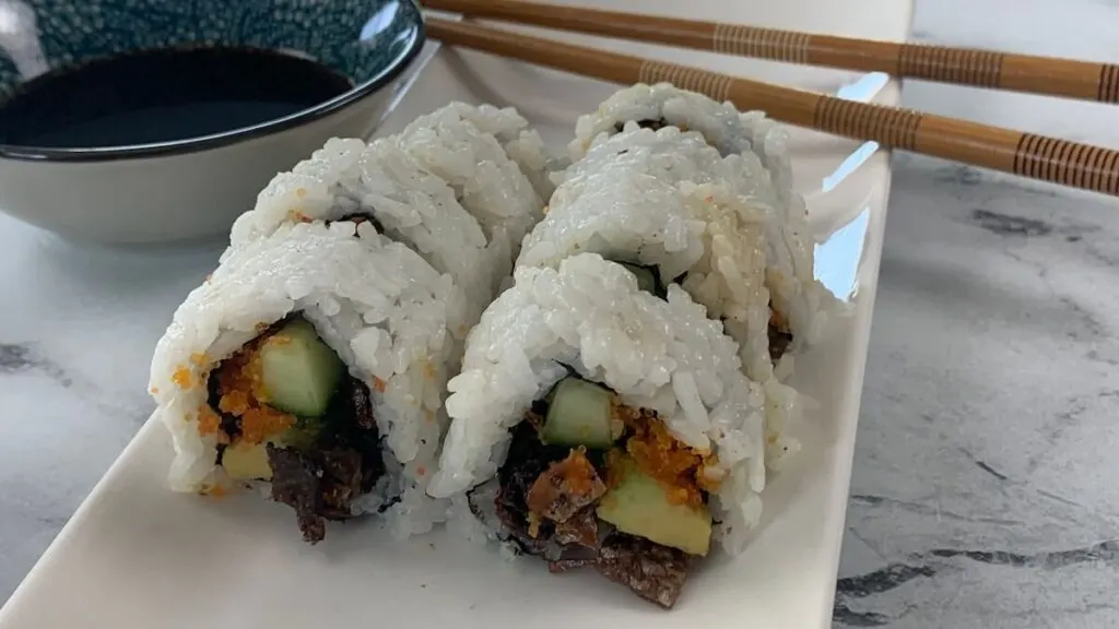 Salmon skin rolls on a white sushi plate with chopsticks and soy sauce in the background.