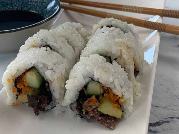 Salmon skin rolls on a white sushi plate with chopsticks and soy sauce in the background.