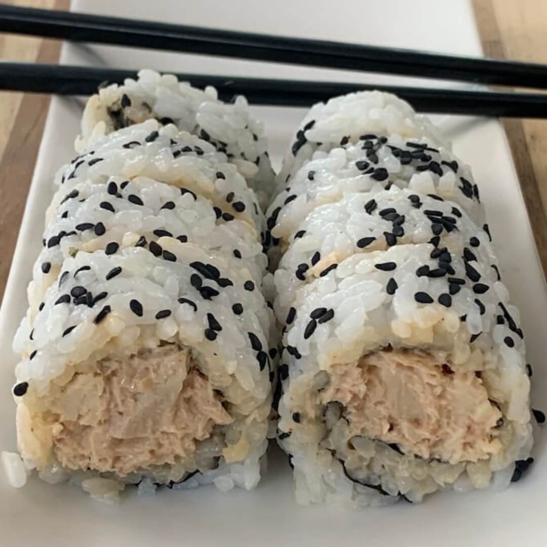 Spicy tuna rolls using cooked tuna on a white sushi plate with black chopsticks in the background.