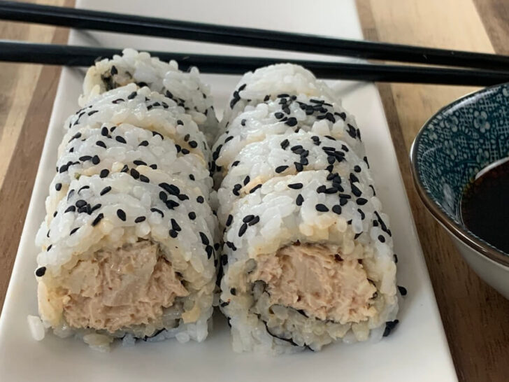 Spicy tuna roll on a white plate with black chopsticks and a ramekin of soy sauce in the background.