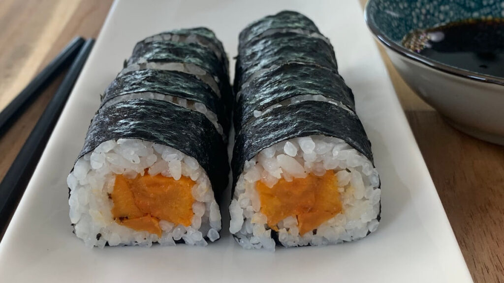 Sweet potato roll sushi on a white platter with chopsticks and a ramekin of soy sauce in the background.