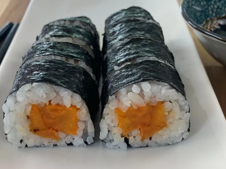 Sweet potato roll sushi on a white platter with chopsticks and a ramekin of soy sauce in the background.