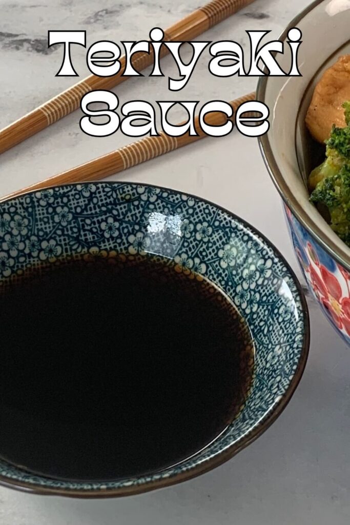 Vertical photo of teriyaki sauce in a Japanese ramekin with a chicken teriyaki bowl and chopsticks in the background.