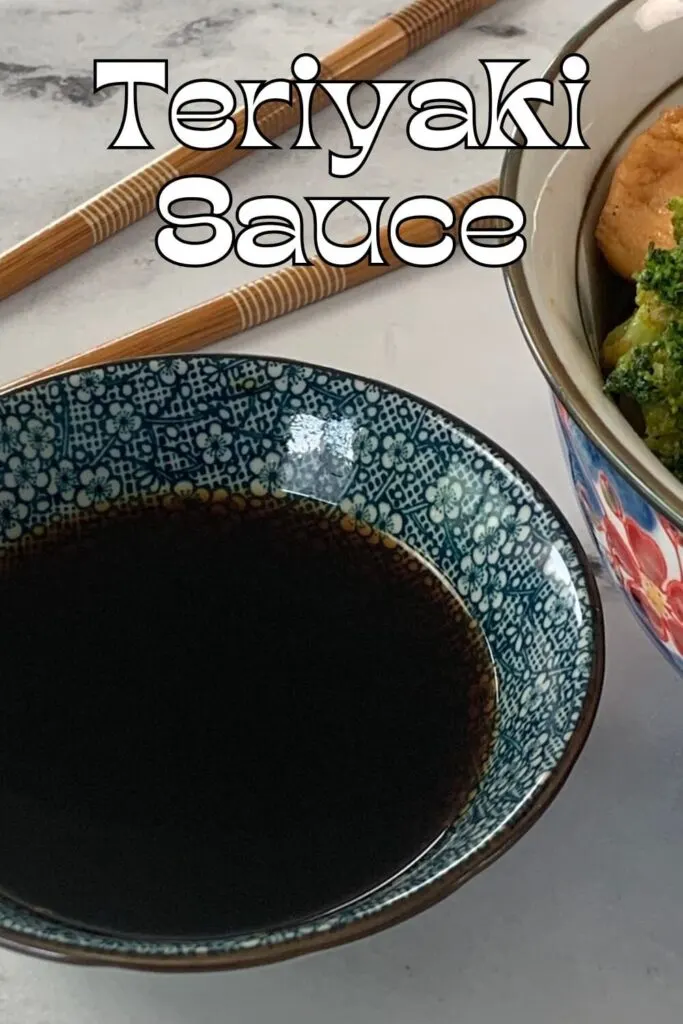 Vertical photo of teriyaki sauce in a Japanese ramekin with a chicken teriyaki bowl and chopsticks in the background.