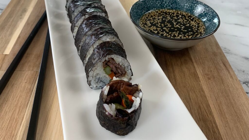 Beef roll sushi horizontal pic on a white sushi platter with yakiniku sauce in the background. 