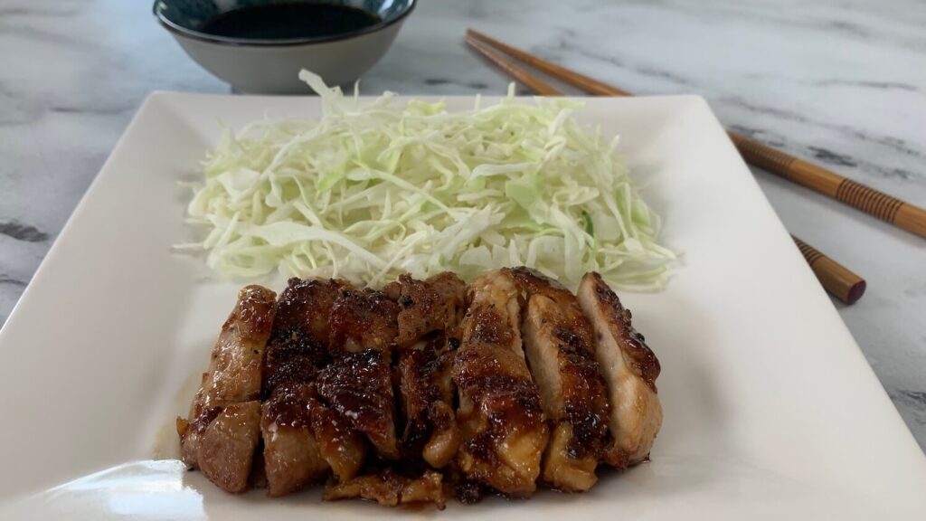 Chicken teriyaki with a bed of coleslaw and a ramekin of teriyaki sauce.