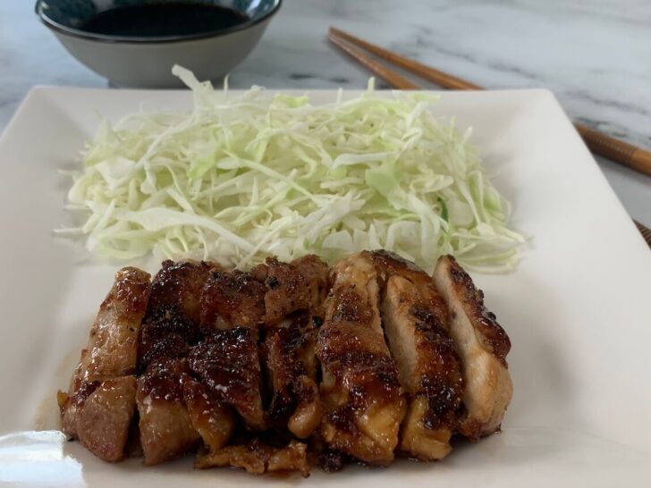 Chicken teriyaki on a white plate with a bed of coleslaw and a ramekin of teriyaki sauce.