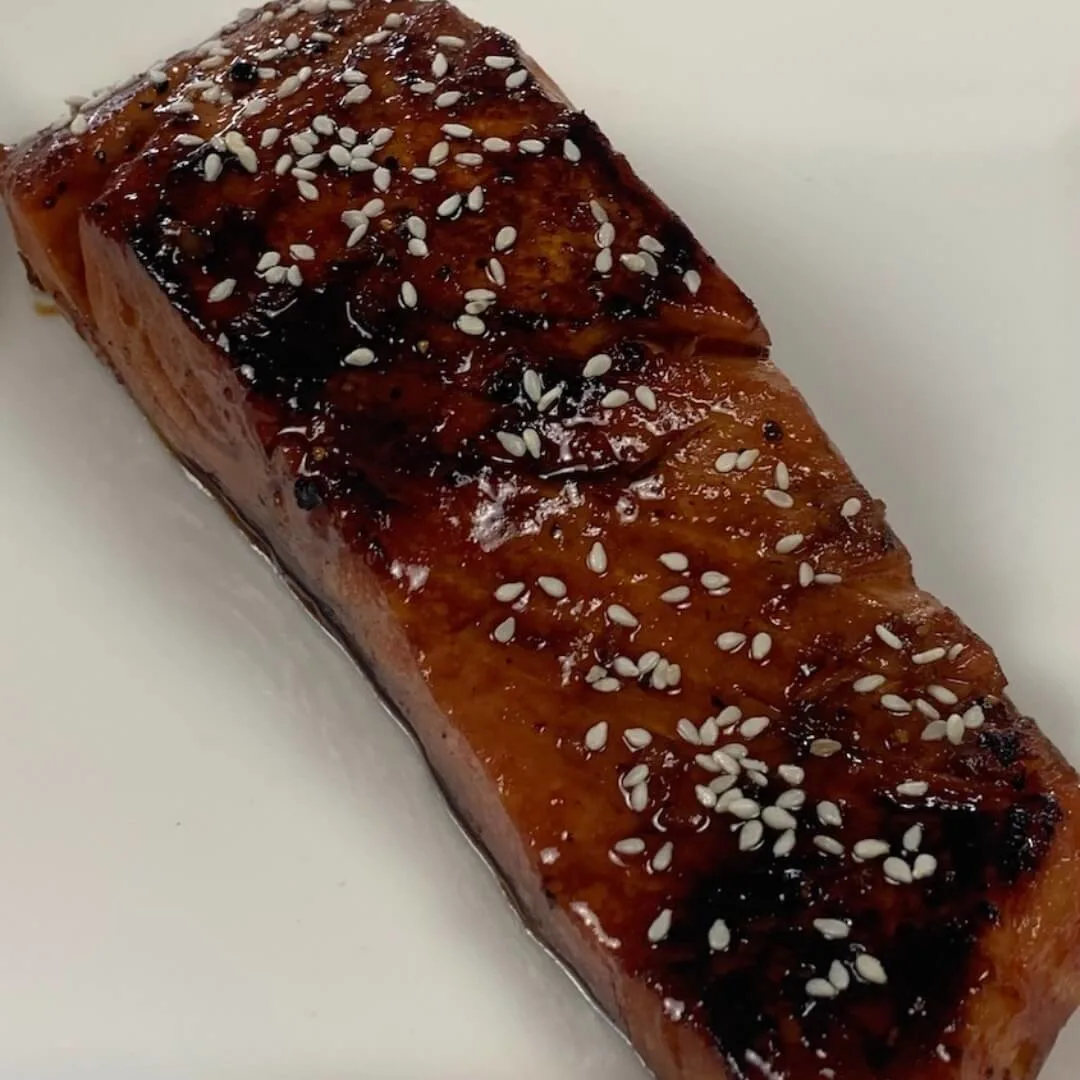 Teriyaki Salmon square pic garnished with white sesame seeds on a white plate.