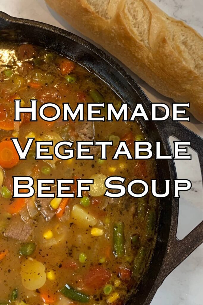 Homemade vegetable beef soup in a cast iron pot with a loaf of bread in the background.